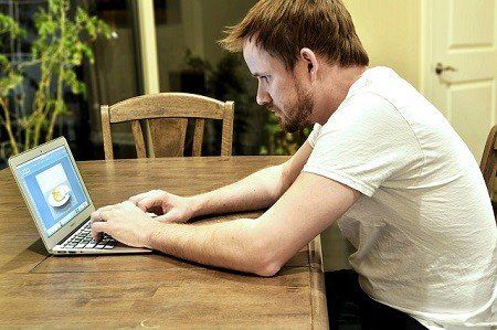 A man is sitting at a table using a laptop computer.